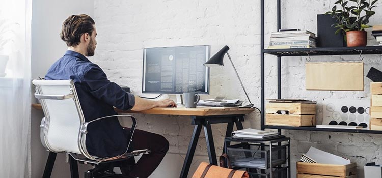 Homem sentado em frente a um computador, com postura confortável e sorridente, representando a importância de uma boa ergonomia no home office para a implementação de práticas de Segurança e Saúde no Trabalho (SST) em Pequenas e Médias Empresas (PMEs)."