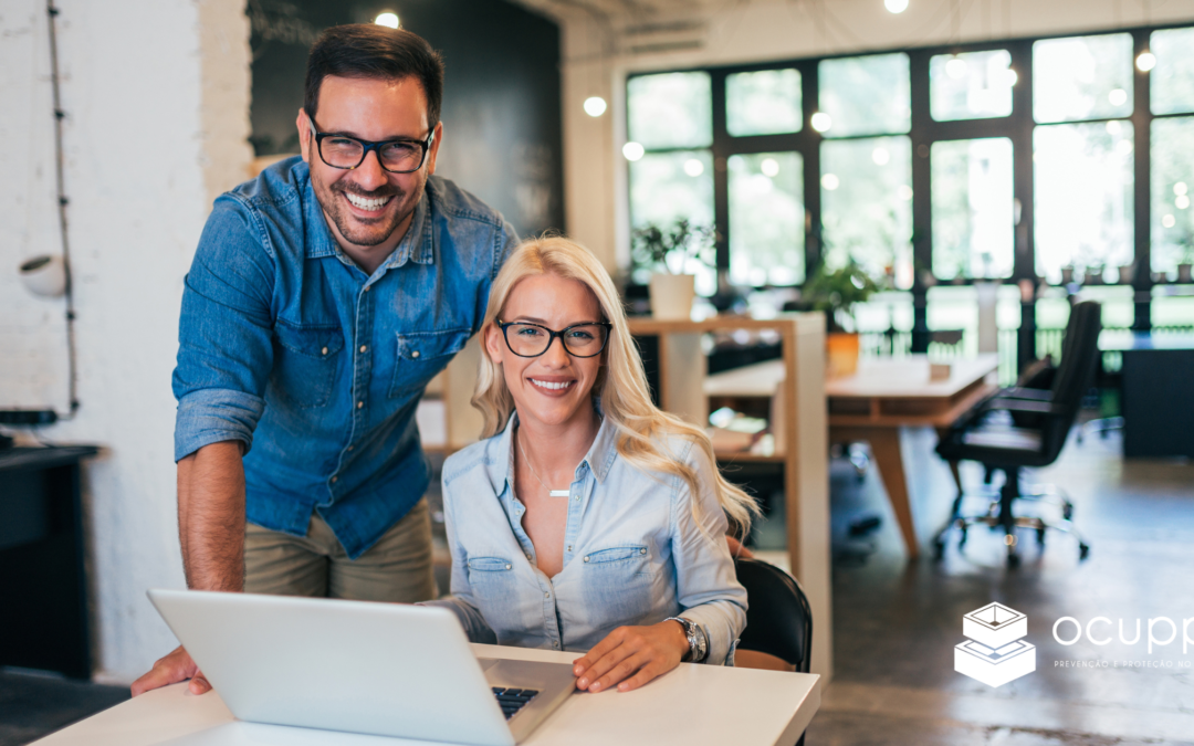 Casal de empreendedores, homem e mulher, sorridentes enquanto olham para um computador, simbolizando o início da implementação de uma cultura de Segurança e Saúde no Trabalho (SST) em Pequenas e Médias Empresas (PMEs).